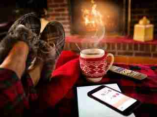 Warm up your home: person sitting at sofa with a hot drink in front of a fire.